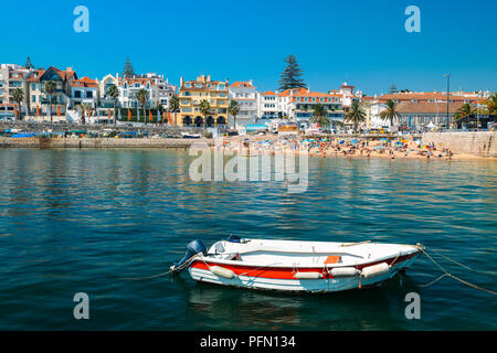 Cascais, Portugal - August 21, 2018: Fishing boat on foreground with crowded sandy beach in Cascais near Lisbon, Portugal during the summer Stock Photo