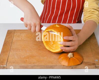 Girl using knife to cut holes in hollowed-out pumpkin, close-up Stock Photo