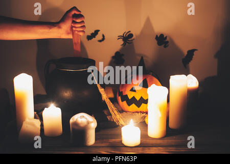 Happy Halloween. witch hand boiling potion for spell, with jack o lantern pumpkin with candles, bowl,broom and bats, ghosts on background in dark spoo Stock Photo