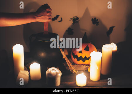 Happy Halloween. witch hand boiling potion for spell, with jack o lantern pumpkin with candles, bowl,broom and bats, ghosts on background in dark spoo Stock Photo