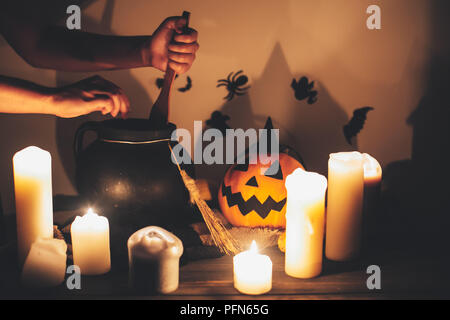 Happy Halloween. witch hand boiling potion for spell, with jack o lantern pumpkin with candles, bowl,broom and bats, ghosts on background in dark spoo Stock Photo