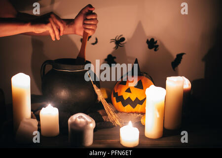 Happy Halloween. witch hand boiling potion for spell, with jack o lantern pumpkin with candles, bowl,broom and bats, ghosts on background in dark spoo Stock Photo