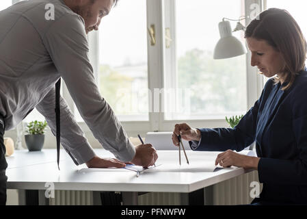 Woman discussing on construction plan with co-worker using pencil and compass. Stock Photo