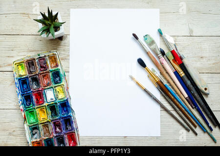 Artist paint brushes and watercolor paintbox on wooden background with empty sheet of paper. Instruments and tools for creative leisure. Paintings art Stock Photo