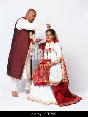 Hindu wedding ritual called sindoor daan, groom sprinkling vermilion powder into parting of bride's hair, close-up Stock Photo
