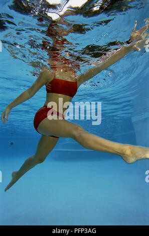 Woman in red swim wear, body submerged in water, with legs outstretched, underwater shot Stock Photo