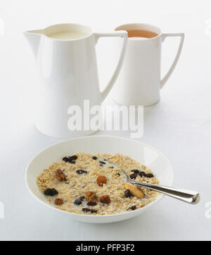 Muesli, containing nuts, seeds and raisins, served in white ceramic bowl with whole milk. Stock Photo