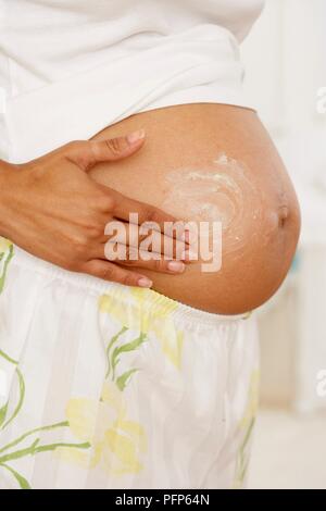 Pregnant woman applying moisturiser on her belly, close-up Stock Photo