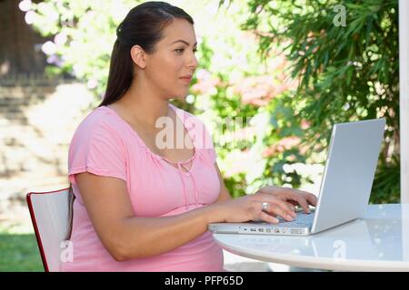 Pregnant woman using laptop in garden Stock Photo