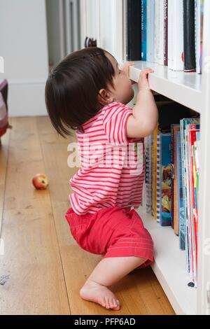 Baby girl pulling herself up on bookshelf, side view Stock Photo