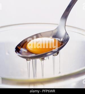 Egg yolk in slotted spoon being separated from the white, close-up Stock Photo