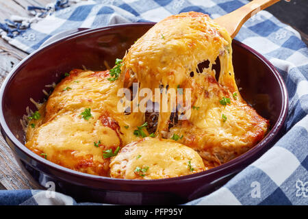 Pork Chop Topped with Onions, Mayo and  stringy melted Cheese on a wooden spoon in a baking dish on a old dark wooden table, view from above, close-u Stock Photo