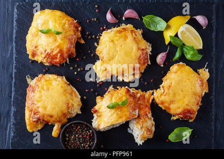Pork Chops Topped with Onions, Mayo and stringy melted Cheese on a black slate plate on a wooden table, view from above, close-up Stock Photo