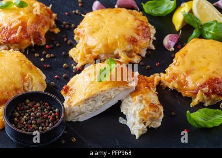 close-up of  Pork Chops Topped with finely chopped Onions, Mayo and melted Cheese on a black slate plate on a wooden table, horizontal view from above Stock Photo