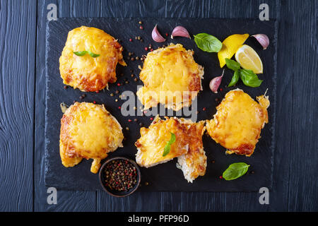 close-up of Pork Chops Topped with finely chopped Onions, Mayo and melted Cheese on a black slate plate on a wooden table, horizontal view from above, Stock Photo