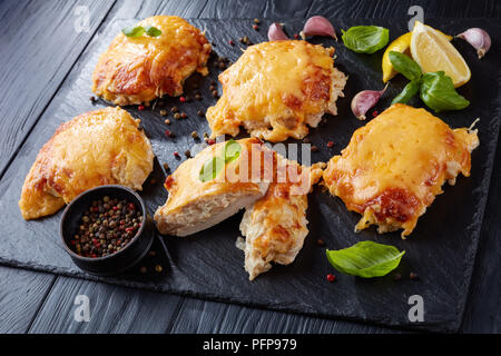 close-up of Pork Chops Topped with finely chopped Onions, Mayo and melted Cheese on a black slate plate on a wooden table, horizontal view from above Stock Photo