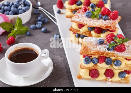 french dessert millefeuille of puff pastry and custard cream, raspberries, blueberries on a plate with cup of coffee and berries on a table, view from Stock Photo