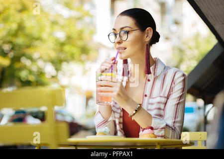 Young woman drinking cold lemonade and touching a sipping straw Stock Photo