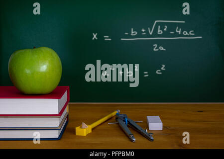 Mathematics class concept with green apple on pile of books and drawing compass with equation on blackboard Stock Photo