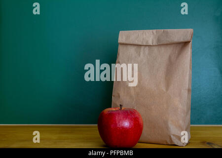 School lunch. Brown paper bag and a red apple on top of wooden desk Stock Photo