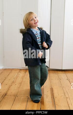 Blonde haired boy smiling, wearing coat indoors Stock Photo