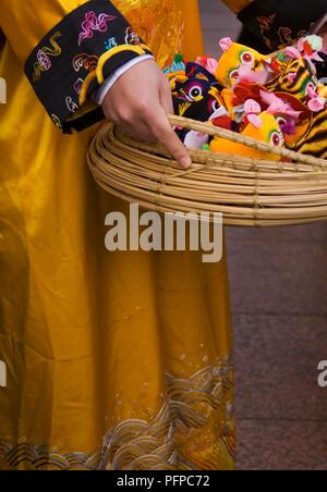 England, London, Soho, Chinatown, young woman in traditional Chinese clothing holding basket of soft toy talismen Stock Photo