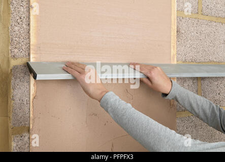Hands running feather edge down plaster on wall Stock Photo