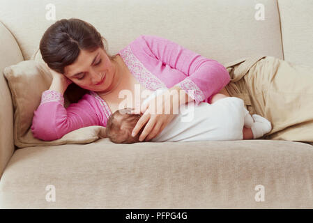 Woman breastfeeding baby boy (4 weeks), lying down on sofa Stock Photo