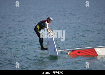 Young man in wet suit and life jacket, standing on daggerboard of capsized dinghy Stock Photo