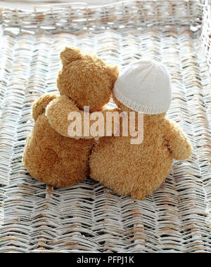 Two teddy bears on wicker surface, one with a woolly hat on Stock Photo