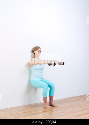 Woman practising Palates with dumbbells against wall Stock Photo