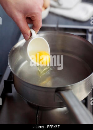 Sliding egg from cup into hot water (cooking poached eggs) Stock Photo