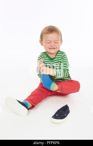 Little boy in green stripey top sitting, taking off shoes and socks  (Model age - 22 months) Stock Photo