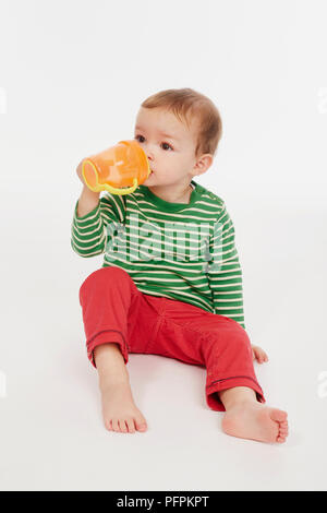 Little boy in green stripey top drinking from beaker (Model age - 22 months) Stock Photo
