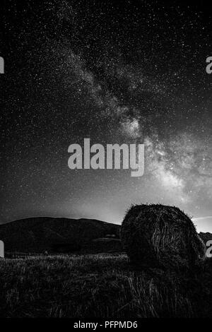 Beautiful view of starred night sky with milky way over a cultivated field with hay bale Stock Photo