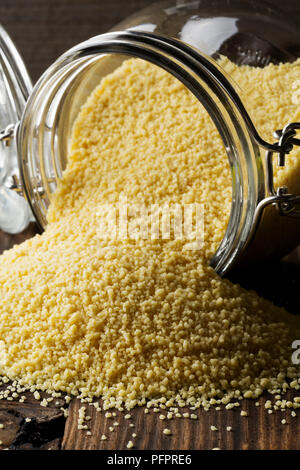 Heap of raw, uncooked couscous in glass jar on wooden table background Stock Photo