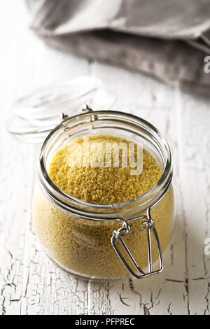 Heap of raw, uncooked couscous in glass jar on white wooden table background Stock Photo