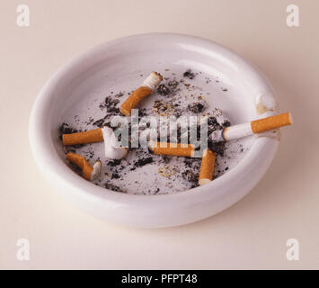 rim cigarette White circular ashtray with cigarette butts and lit cigarette resting on  the rim, close up Stock Photo