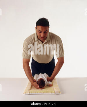 Father supporting head of newborn baby lying on back on changing mat Stock Photo
