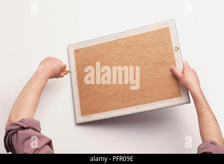 Man making holes in picture frame using an awl Stock Photo