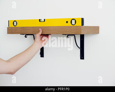 Man holding spirit level on shelf attached to white wall, close-up Stock Photo
