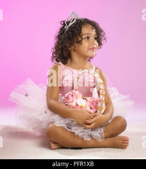 Girl in ballerina costume sitting with her legs crossed, holding basket of flowers Stock Photo