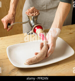 Man using meat grinder to fill sausage casing with minced pork on kitchen table, close-up Stock Photo