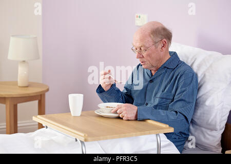Older man sitting up in bed and eating from portable table or overbed table Stock Photo