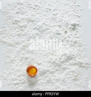 Egg yolk, separated from egg white, in eggshell on flour-covered surface Stock Photo