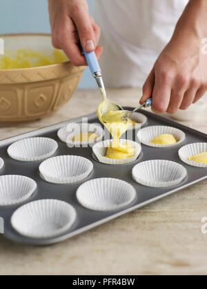Spooning cupcake mixture into paper cases Stock Photo