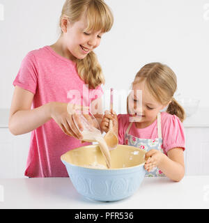 Girls pouring yeast and water mixture into bowl of flour, 5 years and 9 years Stock Photo