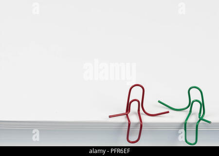 Paper clips red and green sitting on a white paper ream and talking or having a conversation. A photo with a copy space. Good for business meeting, of Stock Photo