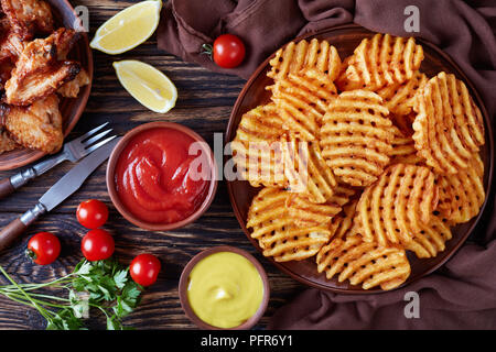 fried chicken wings and Crispy Potato Criss Cross Fries on a clay plates on a wooden table with mustard and tomato sauce dipping, view from above, fla Stock Photo