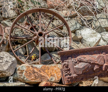 Rusty vintage vehicle wheel and scrap metal on rocks Stock Photo